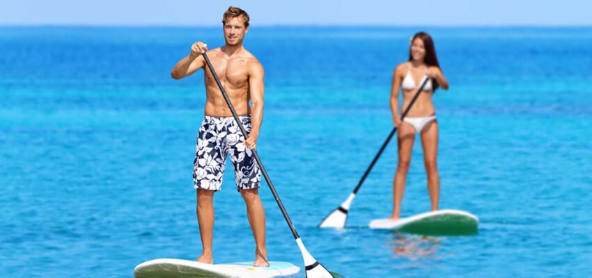 Couple stand up paddleboarding on clear turquoise ocean water under sunny skies, representing the Best Places to Paddleboard in Maui for adventure and relaxation.