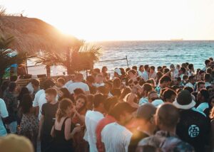  A crowd of people enjoys live Music at Beach Bars at sunset, with vibrant colors illuminating the sky and silhouettes of individuals.
