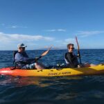 Two people paddling a kayak on the Maui ocean, surrounded by blue water and a clear sky.