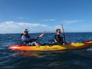 Two people paddling a kayak on the Maui ocean, surrounded by blue water and a clear sky.