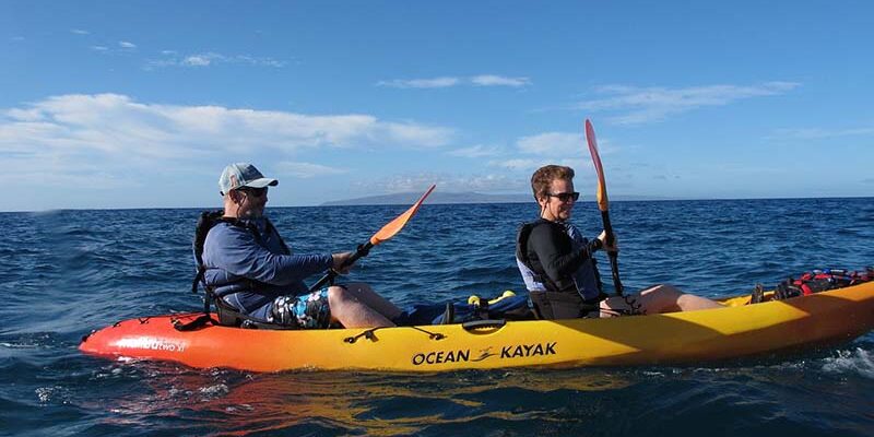 Two people paddling a kayak on the Maui ocean, surrounded by blue water and a clear sky.