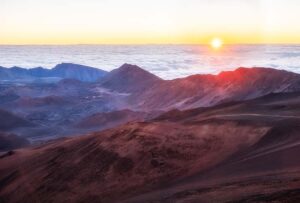 A Watch the Sunrise at Haleakalā illuminates the mountains in the distance, creating a serene and picturesque scene.