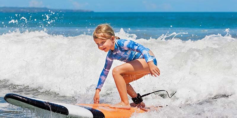 A young girl learning to surf in Maui for beginners, riding ocean waves and enjoying a sunny beach day.